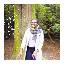 Person wearing glasses and smiling watching confetti rain down in front of her in a woodland setting