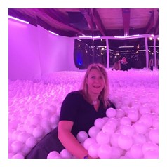 Woman under pink lights laughing in a ball pit filled with white plastic balls